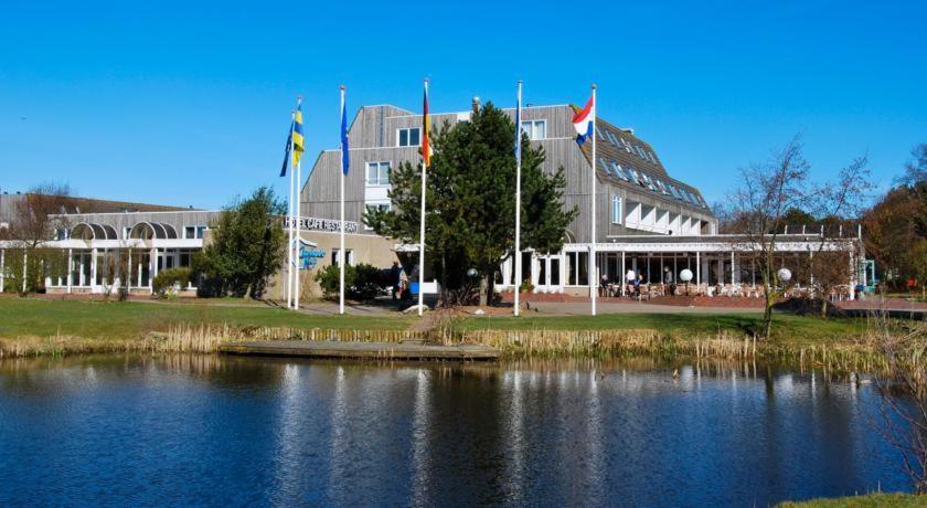 霍勒姆LUXE Appartement ZEEDUIN, Bgg, eigen Terras - volledige KEUKEN- Resort Amelander Kaap, Incl verwarmd Hotel-ZWEMBAD的一座大建筑,在湖前有旗帜