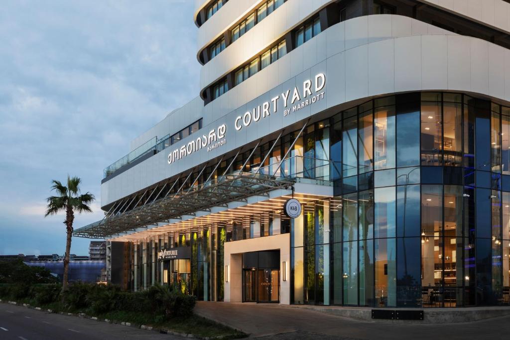 巴统Courtyard by Marriott Batumi的一座大型玻璃建筑,前面有一棵棕榈树