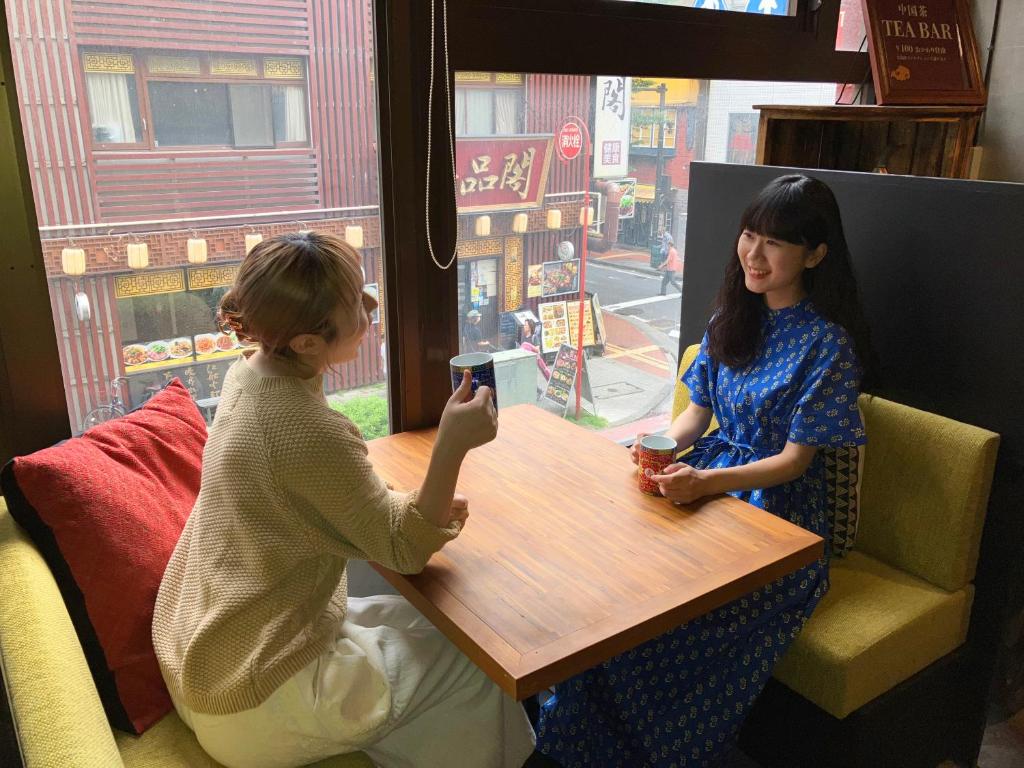 横滨HARE-TABI SAUNA&INN Yokohama的坐在一张桌子旁看手机的两名妇女