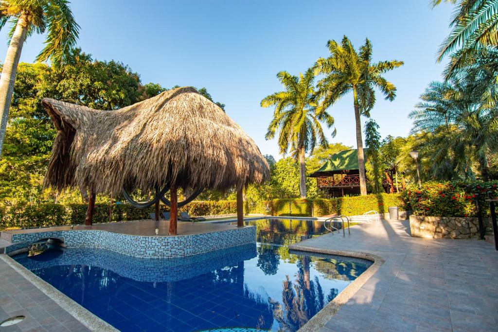 CalabazoPortales del Tayrona Garden Hotel的一个带草伞和棕榈树的度假游泳池