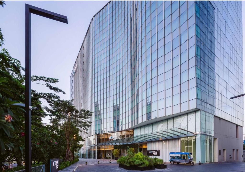 曼谷曼谷名致酒店式服务公寓的一座高大的玻璃建筑,前面有一辆蓝色的卡车