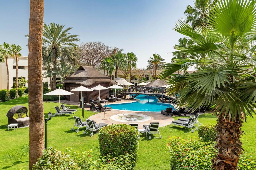 迪拜Le Méridien Dubai Hotel & Conference Centre的一个带游泳池、椅子和棕榈树的度假村