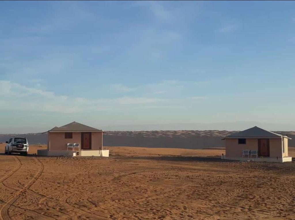 ḨawīyahSafari Dunes Camp的两座房子,旁边停有一辆卡车