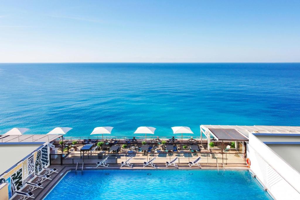尼斯尼斯世贸艾美酒店的一个带椅子和遮阳伞的游泳池以及大海