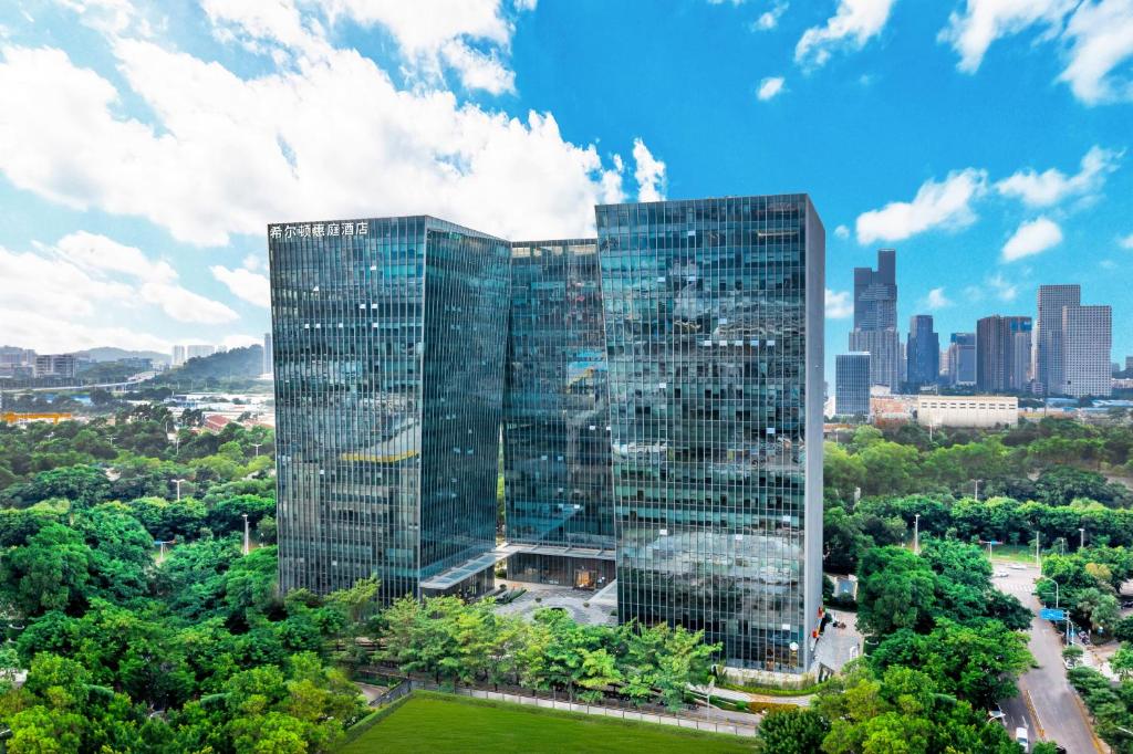 深圳深圳南山科技园希尔顿惠庭酒店的一座高大的玻璃建筑,以城市为背景