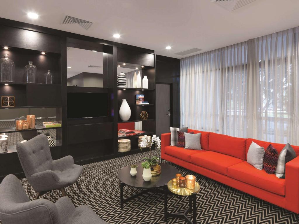 悉尼悉尼机场阿迪纳公寓式酒店的客厅配有红色的沙发和两把椅子