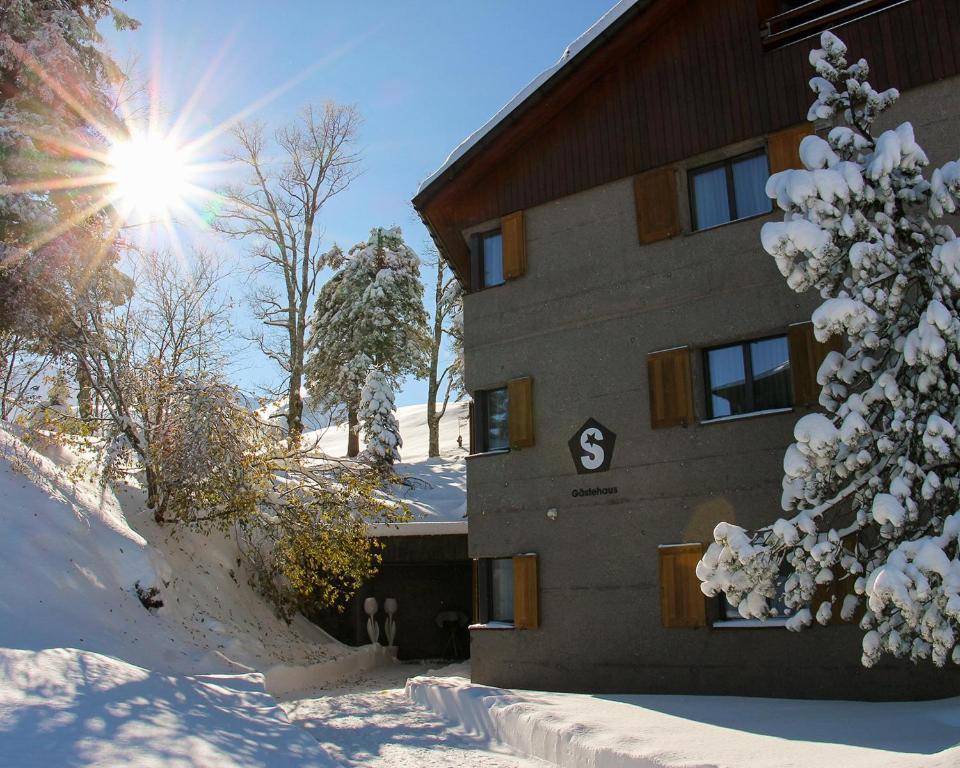 史多斯Gästehaus by Stoos Hotels的雪中的一个建筑,太阳在后面