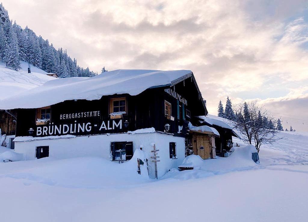 卑尔根Bründling-Alm Berggasthof auf 1167m auf dem Hochfelln的一座被雪覆盖的建筑,上面有标志