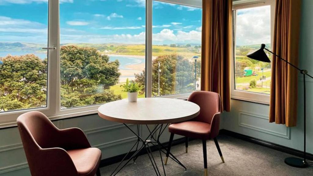 巴利卡斯尔Marine Hotel Ballycastle的配有大窗户的客房内的桌椅