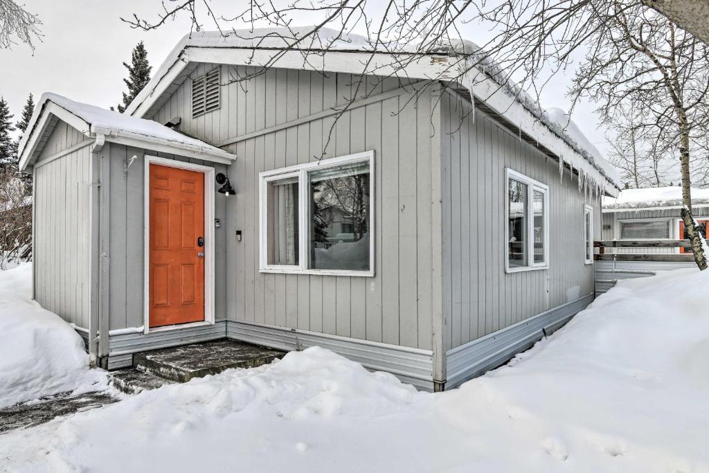 安克雷奇Anchorage Home, Minutes From Downtown!的雪中带橙色门的灰色房子
