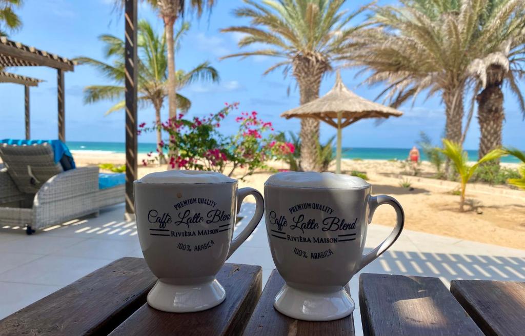 CabeçadasVila Mare - Praia de Chaves frontline的两个咖啡杯坐在海滩附近的木桌旁