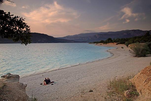 韦尔东的圣克鲁瓦GORGES DU VERDON CAMPING 3 etoiles PROCHE DU LAC DE STE CROIX NBRES ACTIVITES NAUTIQUES RANDONNEES ENTOURE DE CHAMPS DE LAVANDES 4 PERS的一群人躺在海边的海滩上