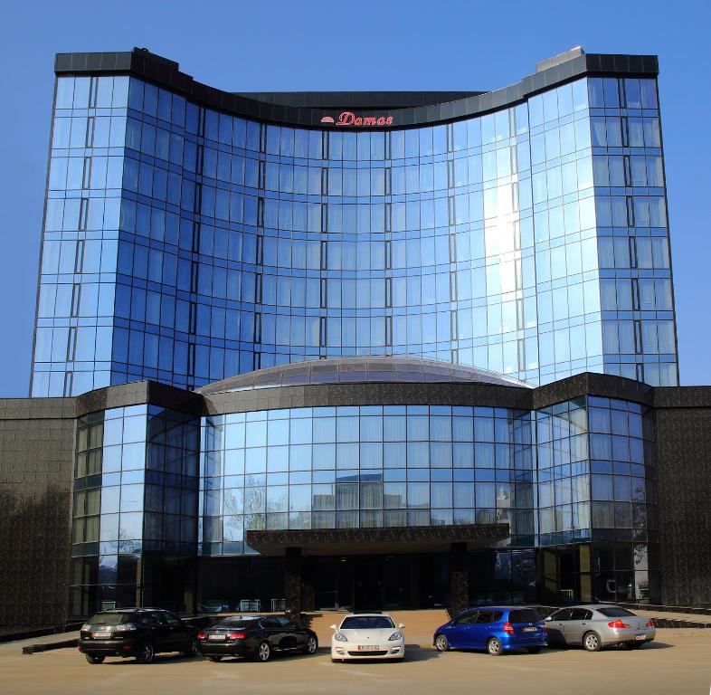 比什凯克达马斯国际酒店的一座大型玻璃建筑,停车场内有车辆停放