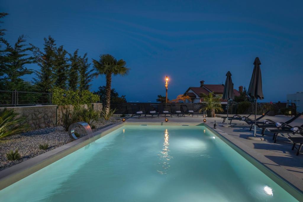 伊齐齐Piccola Villa Adriatic, with heated swimming pool, Opatija的夜间游泳池,配有椅子和遮阳伞