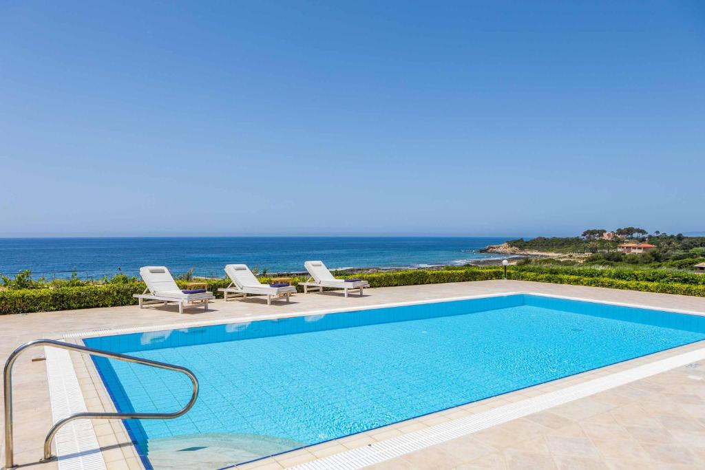 米尼亚Villa Alba Minies的一个带椅子的游泳池,背景是大海