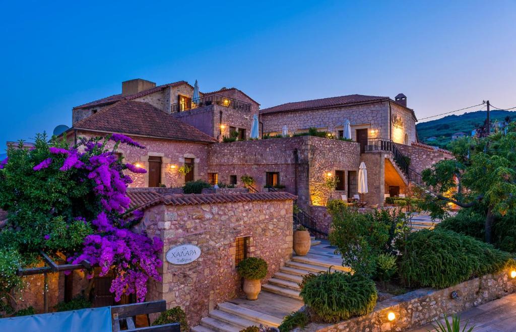 SpiliáSpilia Village Hotel & Villas的一座大石头房子,前面有紫色的鲜花