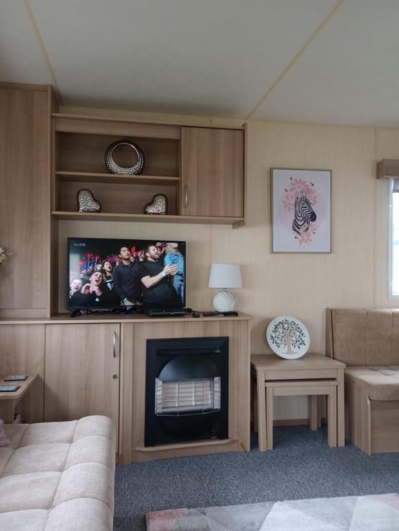 康威A22 is a 3 bedroom caravan on Whitehouse Leisure Park in Towyn near Abergele with decking and close to sandy beach的一间带电视和壁炉的客厅