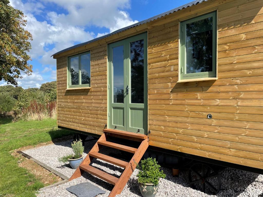 盖尔文Cosy Shepherd Huts near Newborough Forest Anglesey的一座小房子,有绿门和长凳