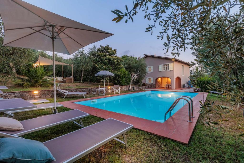 卢卡Villa Dondolino, a Stylish Farmhouse的一个带椅子和遮阳伞的游泳池以及一间房屋