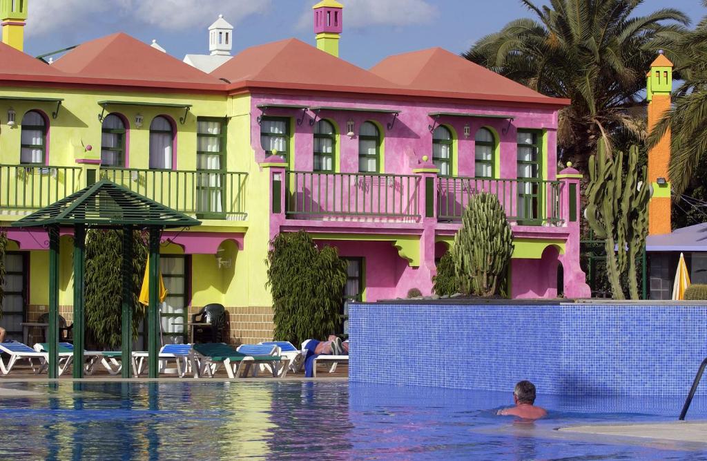 马斯帕洛马斯eó Maspalomas Resort的一个人在建筑物前的游泳池游泳