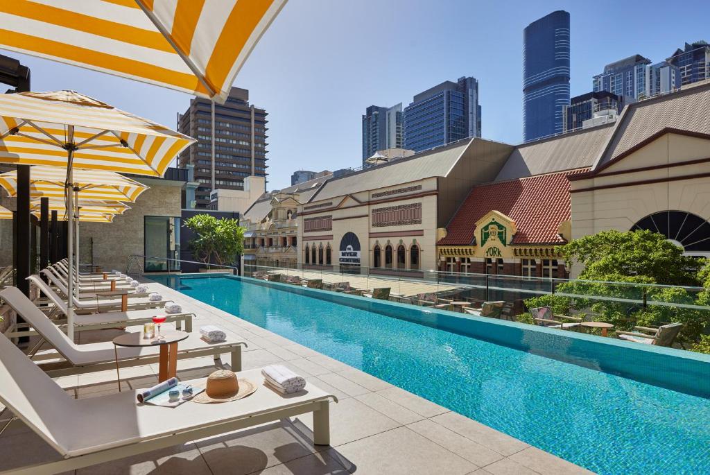布里斯班Hyatt Regency Brisbane的一座带桌子和遮阳伞的游泳池,位于一座建筑旁边