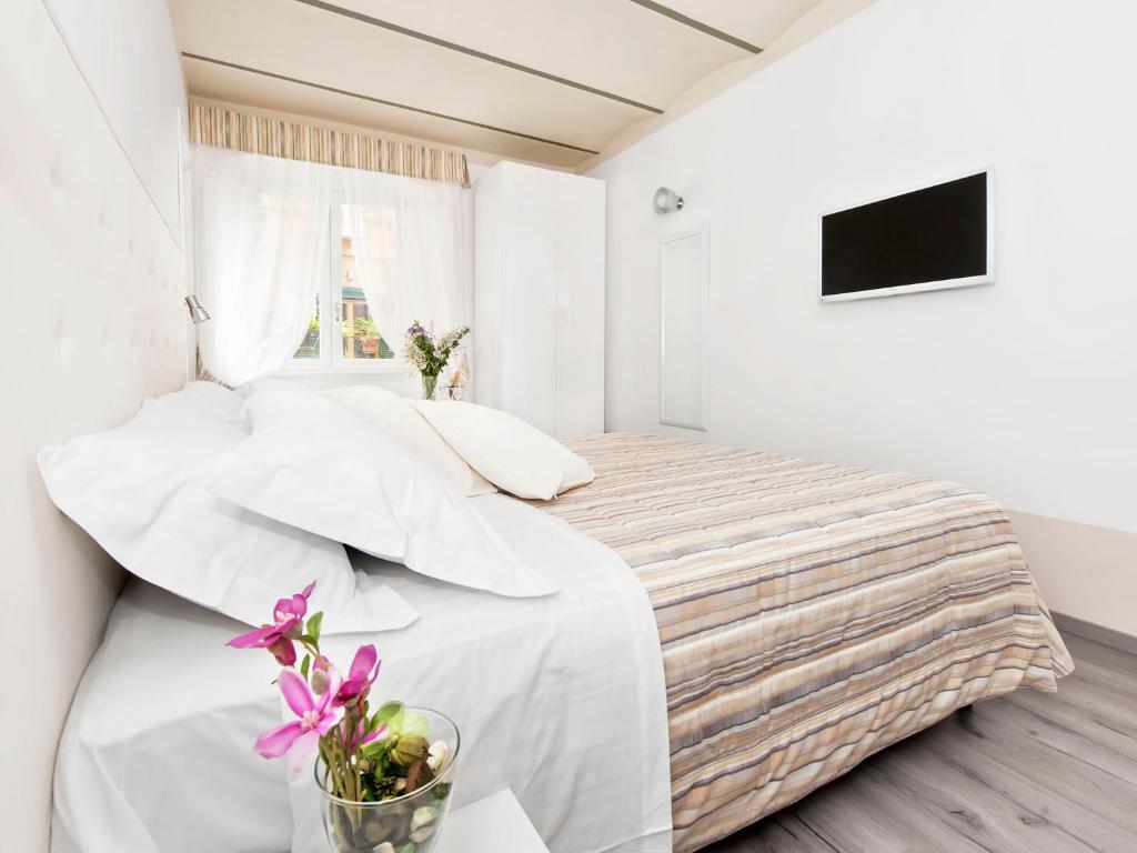 罗马斗兽场白色客房酒店的白色卧室配有一张带白色床单和紫色鲜花的床