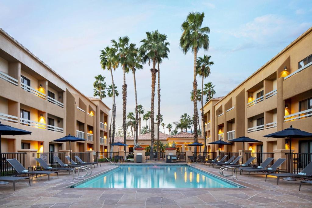 棕榈泉Courtyard by Marriott Palm Springs的一座游泳池,里面摆放着椅子和棕榈树