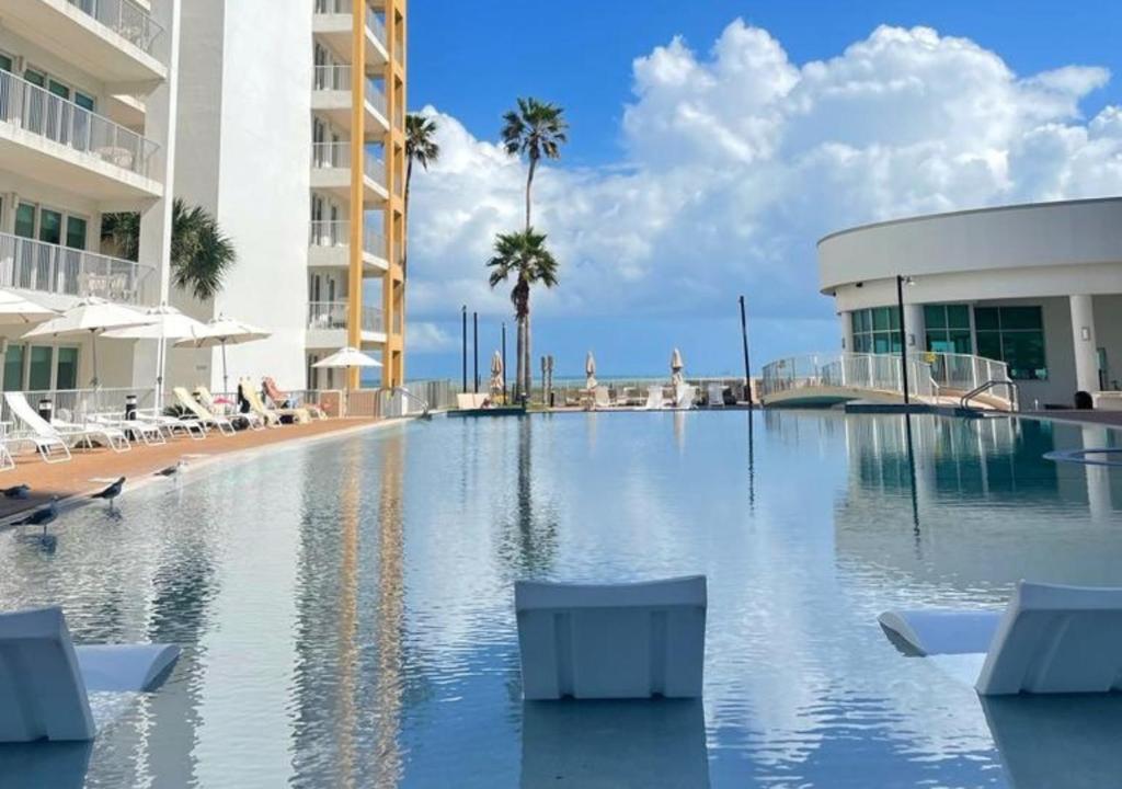 南帕诸岛Peninsula Island Resort & Spa - Beachfront Property at South Padre Island的一个带椅子的游泳池、一座建筑和棕榈树