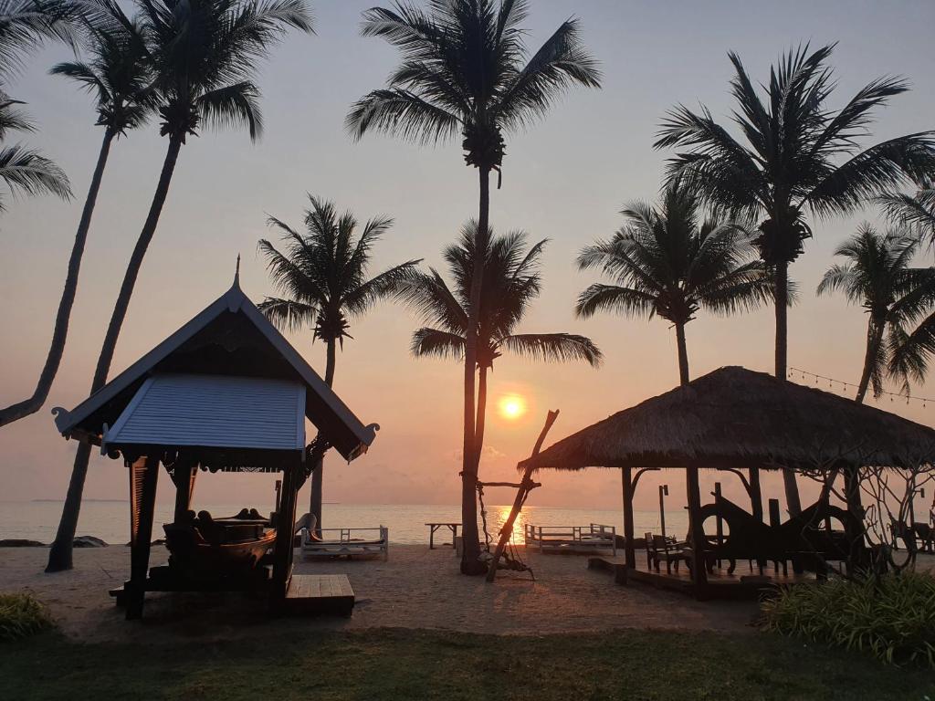 卡农Baan Thong Ching Resort的棕榈树海滩上的日落和小屋