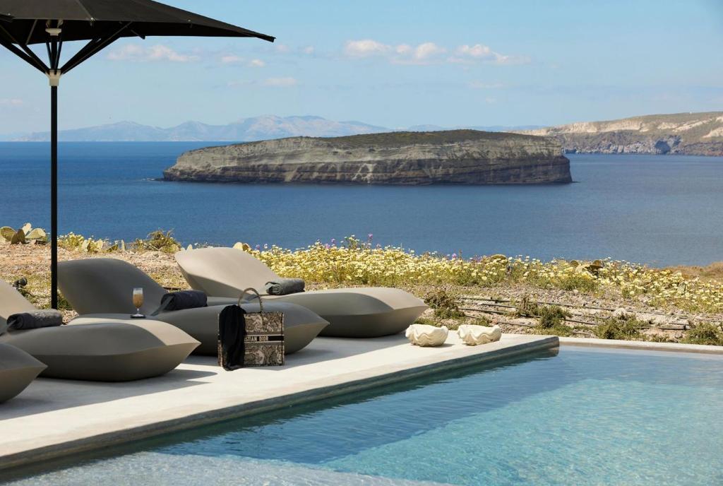 阿克罗蒂里Absolute Paradise Santorini的水边的游泳池配有椅子和遮阳伞