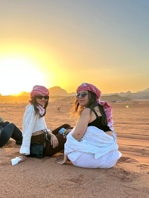 瓦迪拉姆Panorama camp jeep trips的日落时分两个女孩坐在沙漠里