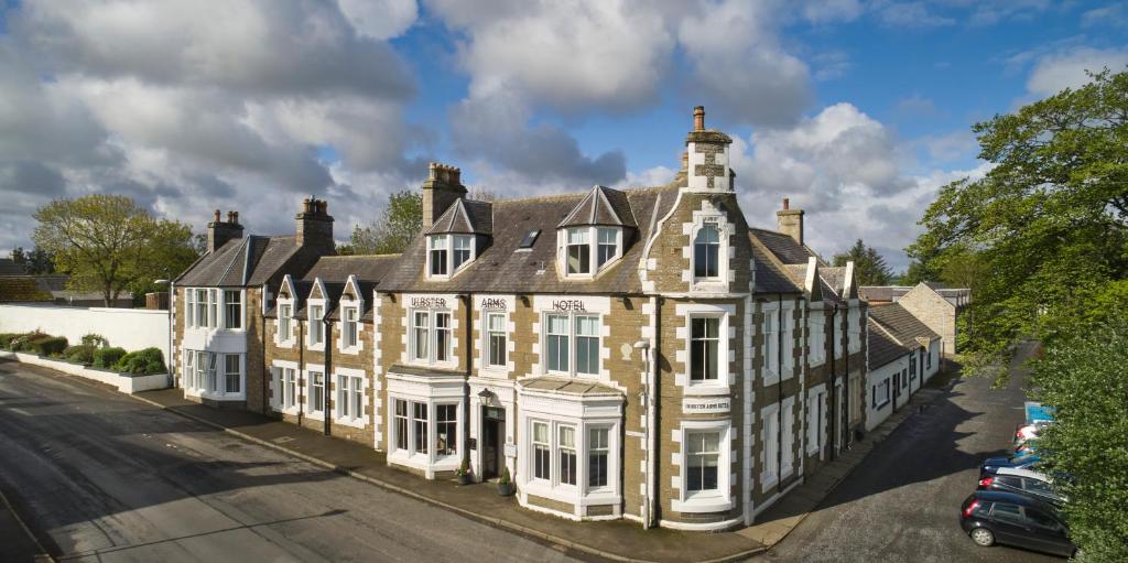 HalkirkUlbster Arms Hotel near Thurso的街上的一栋老房子,前面有停车位