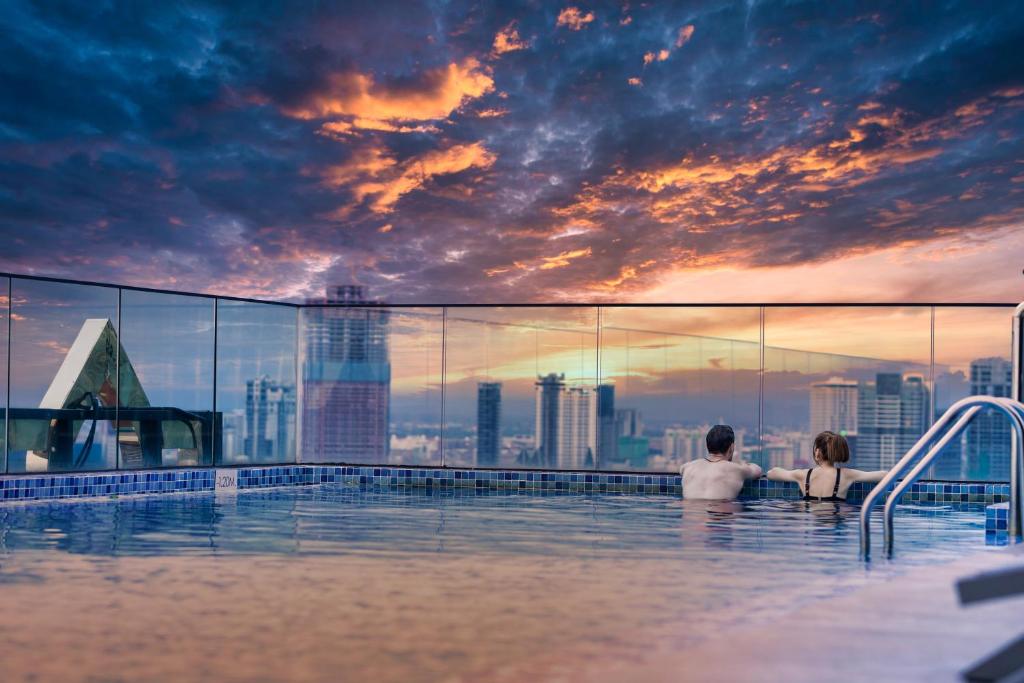 金边Luxcity Hotel & Apartment的城市天际线的无边游泳池中的男女