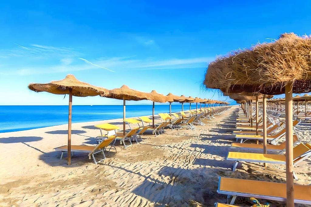 蒂勒尼亚Regina Del Mare Holiday Apartments的海滩上的一排椅子和遮阳伞
