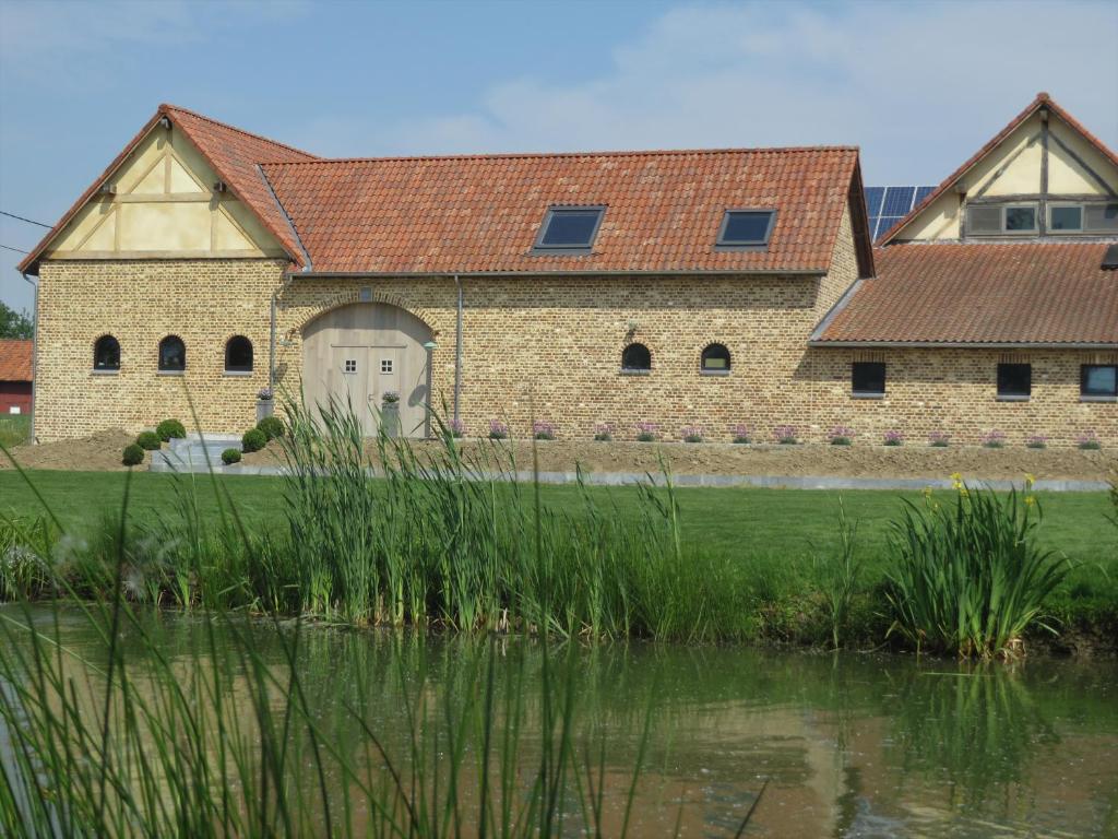 韦伦Hoeve Lavigne的一座大型砖砌建筑,旁边是池塘,有一扇白色门