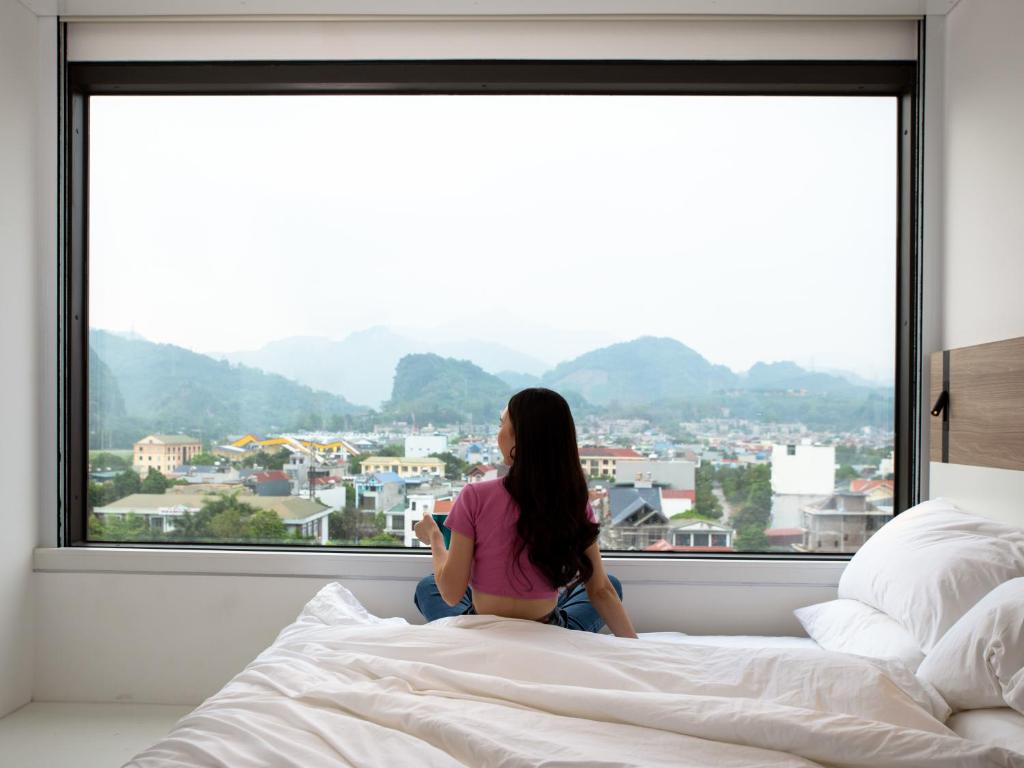 和平SOJO Hotel Hoa Binh的坐在床上,从窗户望出去的女人