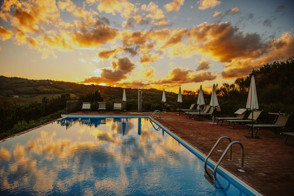 奇尼基亚诺Tenuta Pianirossi的一个带椅子和遮阳伞的游泳池,享有日落美景