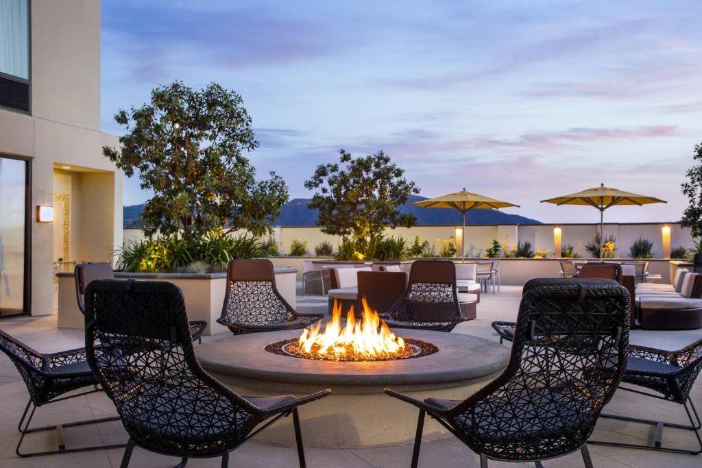 伯班克洛杉矶伯班克/市中心春季山丘套房酒店的露台上的火坑,配有椅子和遮阳伞