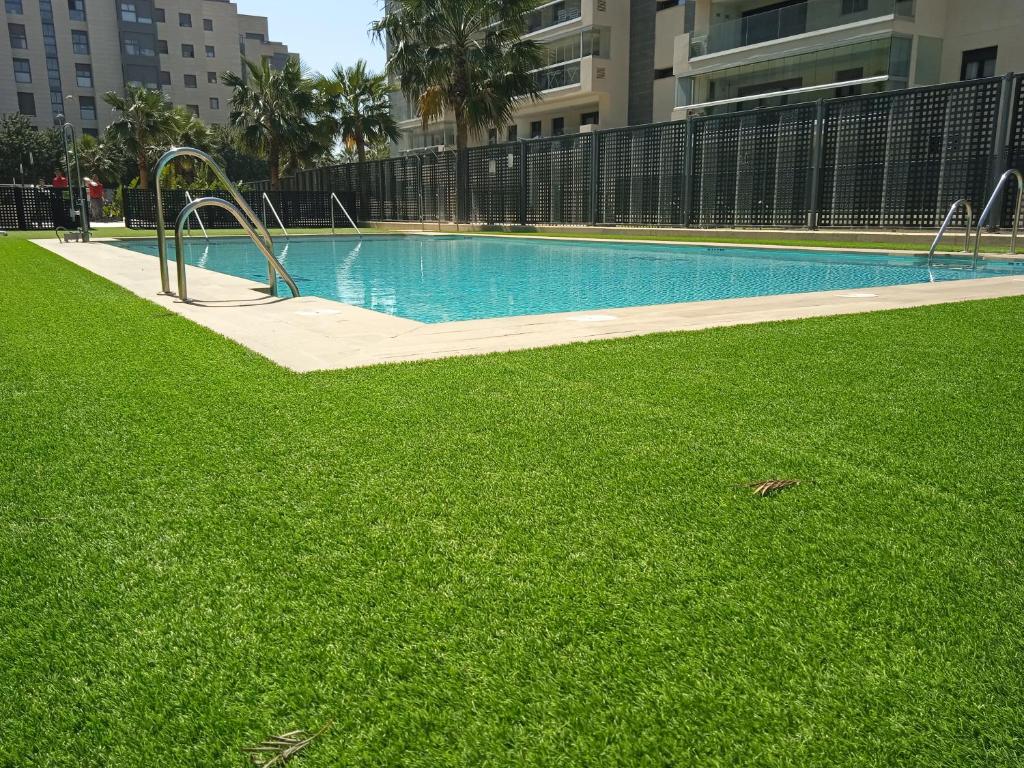 阿尔么丽亚Piso nuevo con piscina cerca de parque las familias y playa de Almeria的一座带绿草的游泳池,位于大楼旁