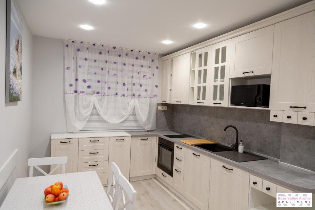 卡赞勒克Rose Valley Aroma Apartment的厨房配有白色橱柜和一张带一碗水果的桌子