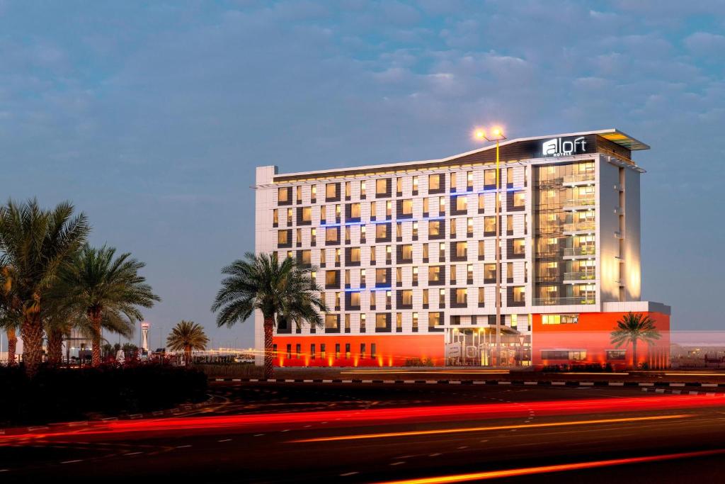 迪拜Aloft Dubai South的一座灯火通明的酒店,前面有棕榈树