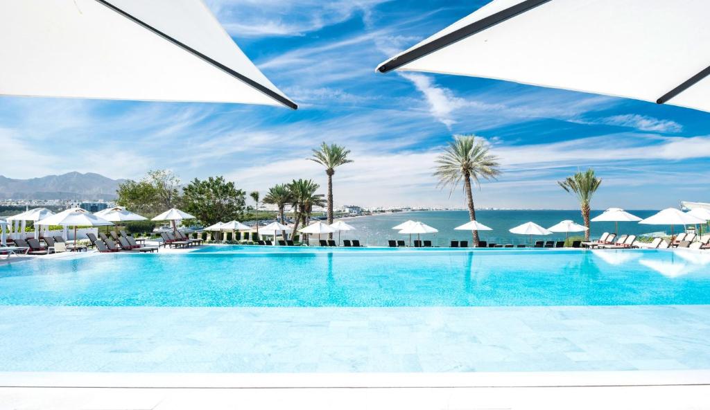 马斯喀特马斯喀特皇冠假日酒店的一座棕榈树和遮阳伞的大型游泳池