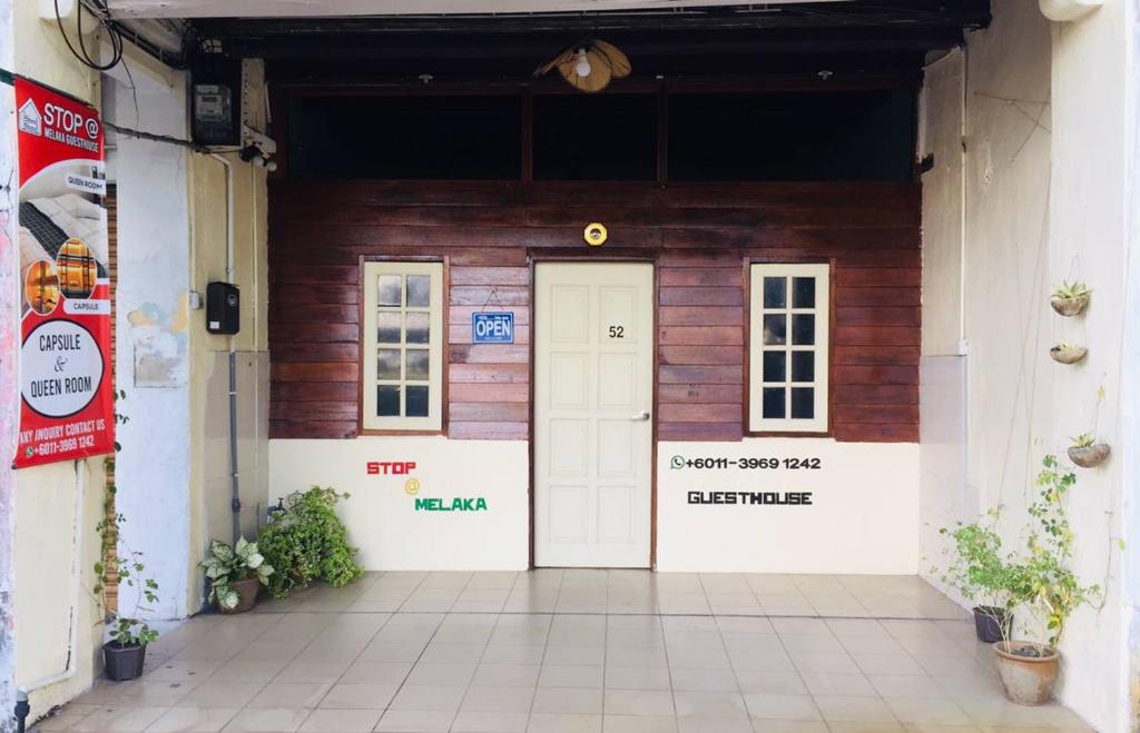 马六甲Stop @Melaka Guesthouse的一座带白色门和2扇窗户的木制建筑