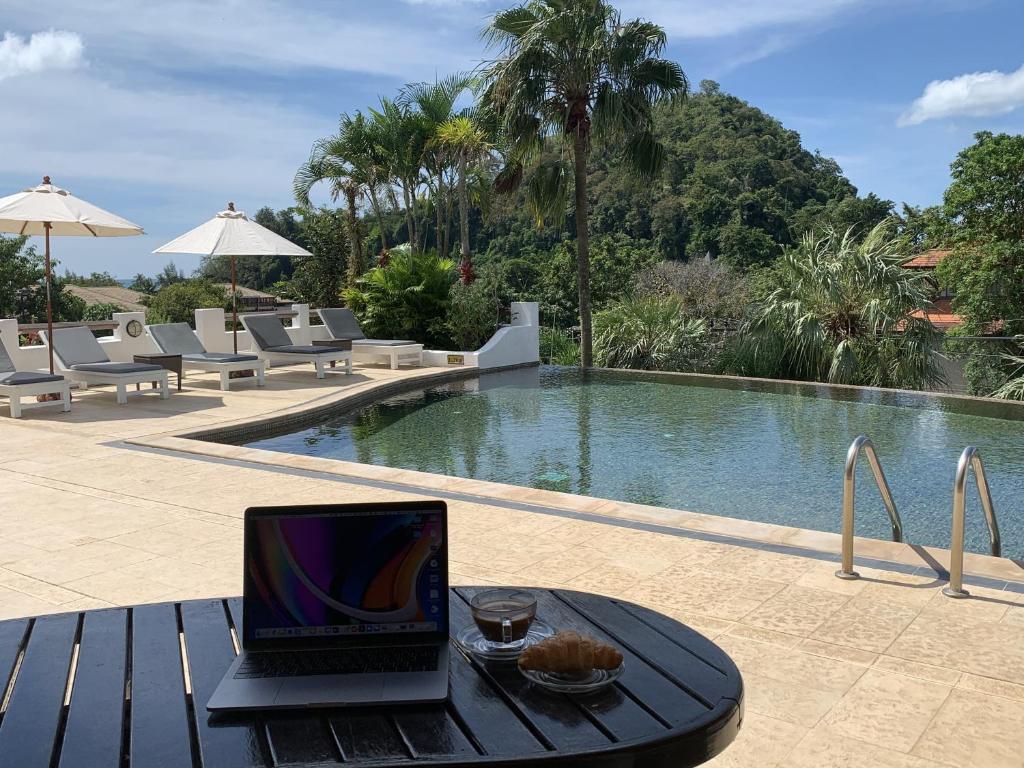 奥南海滩Ao Nang Colors Hotel - Aonang Beach的坐在游泳池旁桌子上的笔记本电脑