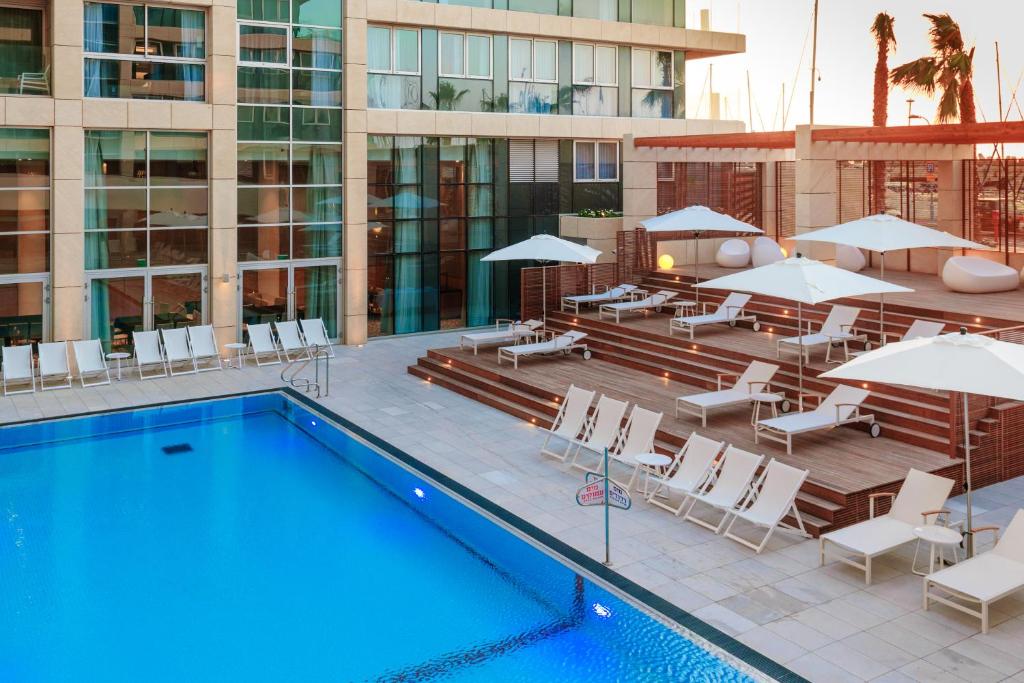 荷兹利亚荷兹利亚希律酒店的一座带椅子和遮阳伞的游泳池位于一座建筑旁边