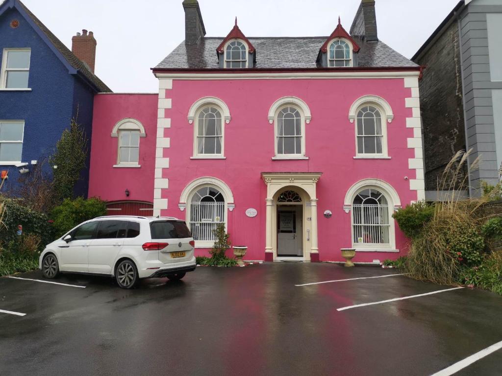 卡迪根Llety Teifi Guest House的停车场内有白色汽车的粉红色房子