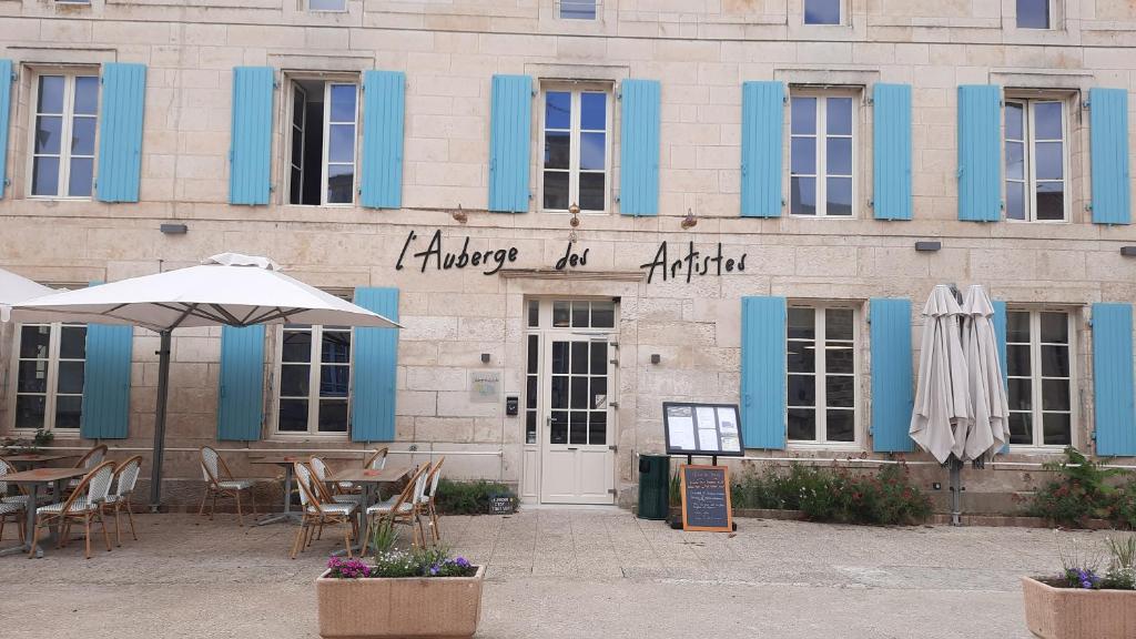 Nieul-sur-lʼAutiseL'Auberge des Artistes的一座带蓝色门、桌子和遮阳伞的建筑