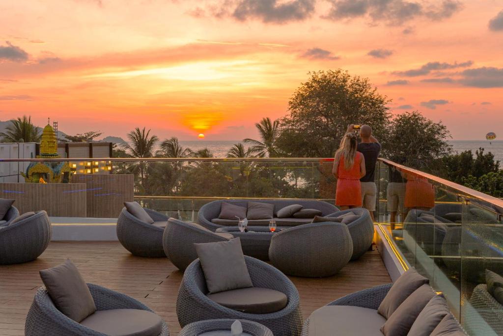 芭东海滩Clarian Hotel Beach Patong的站在阳台的一边欣赏日落的女人