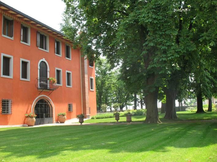 Chiópris-Viscone奇奥里奇别墅 的一座橘色的建筑,有树和草地庭院