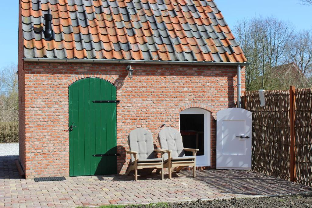 阿赫特克克Trekkershuisje 't Zeeuws Knoopje的砖砌建筑,配有两把椅子和一扇绿门